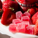 Kush Queen Strawberry THC and CBD gummies with fresh strawberries and Kush Queen Strawberry THC and CBD gummies packaging in the background.
