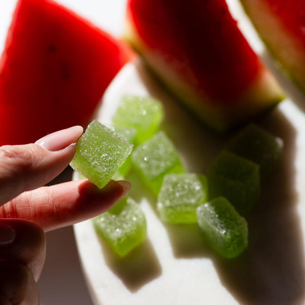 Kush Queen Watermelon THC and CBD gummies being held by a hand with watermelon slices in the background.